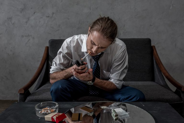 businessman with drug addiction smoking cigarette above table with various drugs